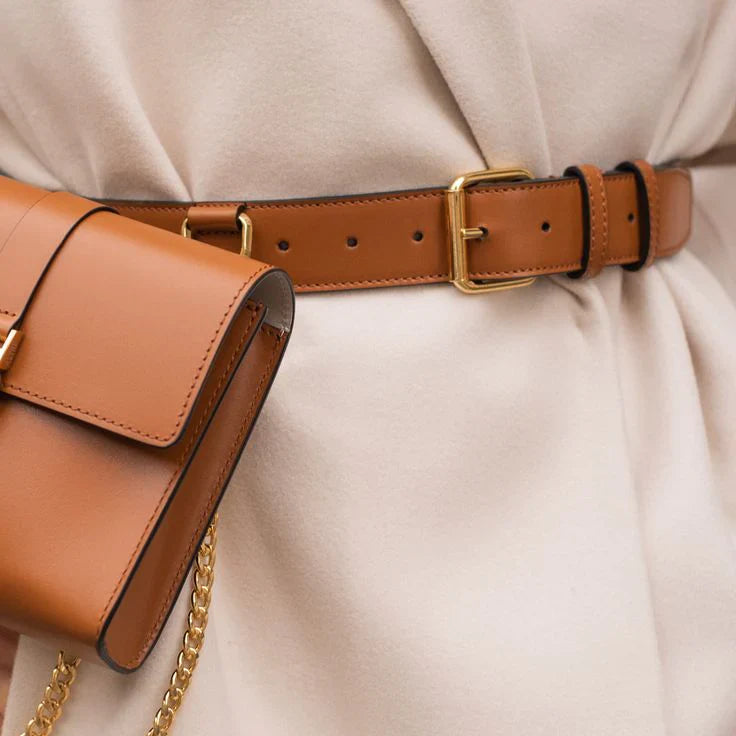 Vue rapprochée d'un sac à main en cuir marron, accompagné d'une ceinture assortie avec une boucle dorée. Les deux accessoires sont portés avec une tenue beige élégante, créant une silhouette chic et sophistiquée.