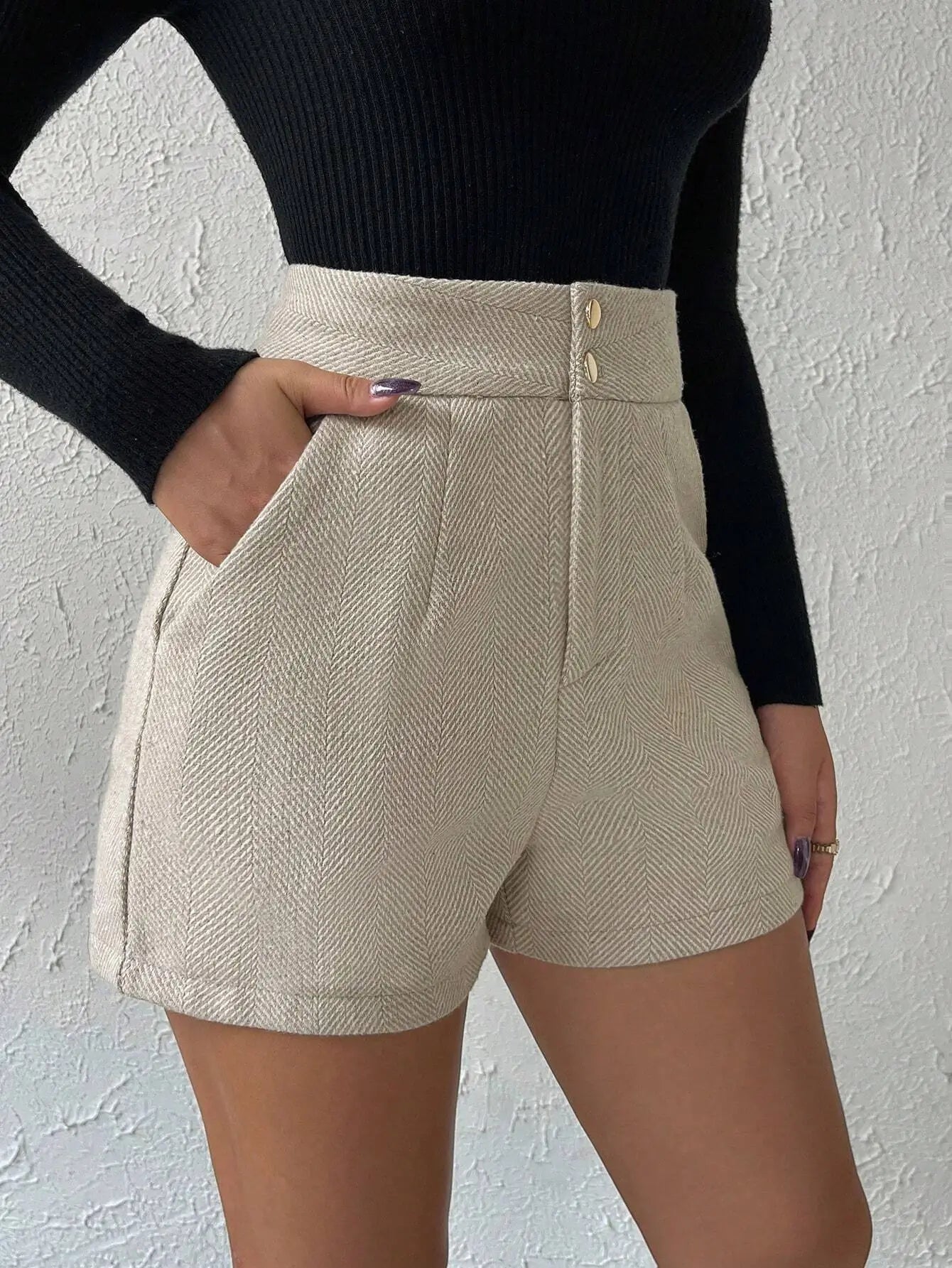 Short à chevrons beige, élégant et sophistiqué. Taille haute ajustée, détails plissés à l'avant, poches latérales et deux boutons dorés à la taille. Confectionné en mélange de fibres naturelles et synthétiques pour une texture structurée. Lavage à la main ou en machine à 30°C recommandé.