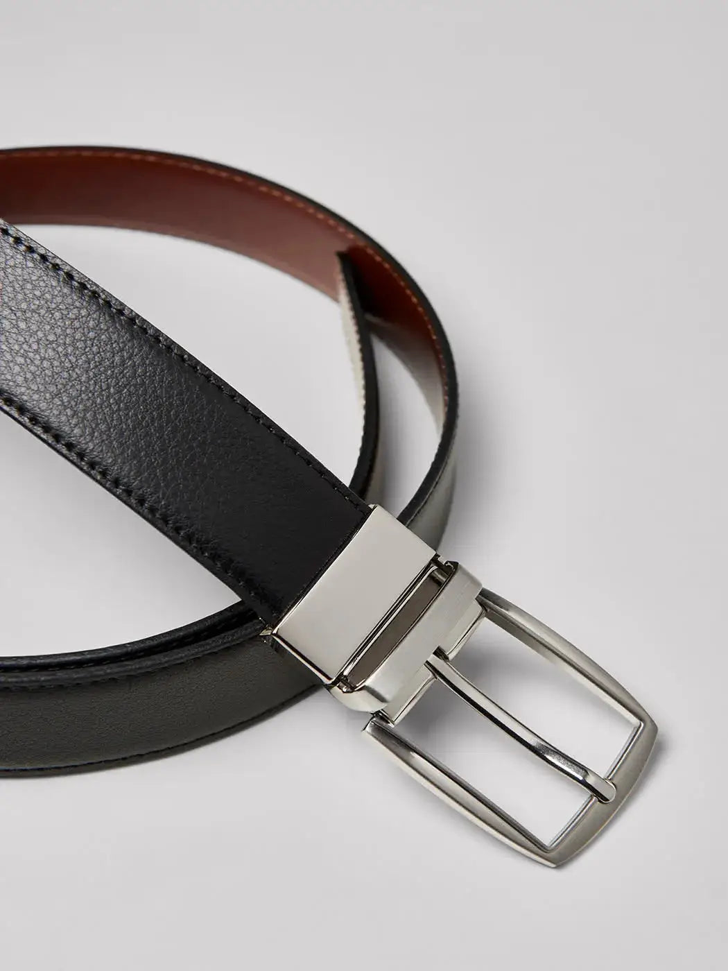 Ceinture réversible en cuir, disponible en noir et chocolat. Composée de croûte de cuir avec une boucle rectangulaire en zamak brossé et des surpiqûres ton sur ton. Largeur de 3,3 cm avec cinq trous d'ajustement. Entretien : éviter lavage, blanchiment, repassage et séchage en machine.