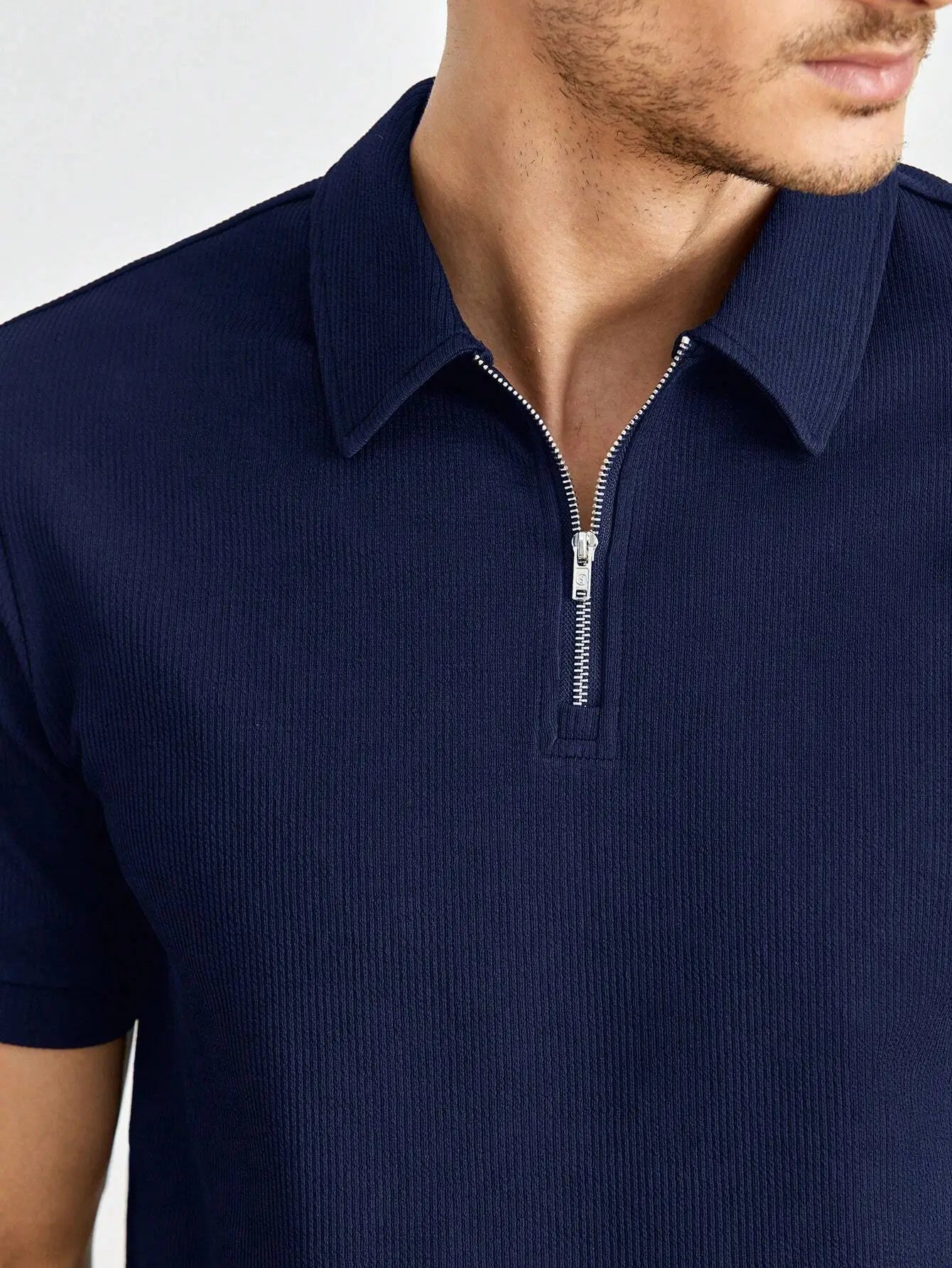 Polo zippé à manches courtes en mélange de coton et fibres synthétiques, alliant confort et respirabilité. Il présente un col polo classique, une fermeture éclair courte et une coupe droite légèrement ajustée. Disponible en bleu marine avec finitions côtelées aux manches et à l'ourlet. Lavage en machine à froid recommandé pour préserver la qualité.