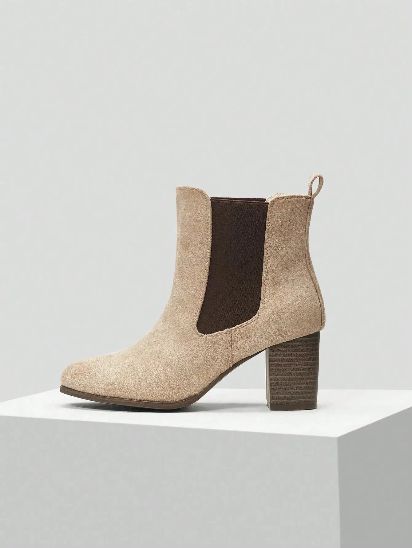 Bottines Chelsea à talon en suédine beige sable, agrémentées d'élastiques latéraux marron foncé. Design épuré à enfiler avec boucle arrière et talon bloc carré de hauteur moyenne. Construction extérieure et doublure en suédine, semelle extérieure en caoutchouc, semelle intérieure en similicuir. Style minimaliste et polyvalent. Entretien : nettoyage à sec recommandé.