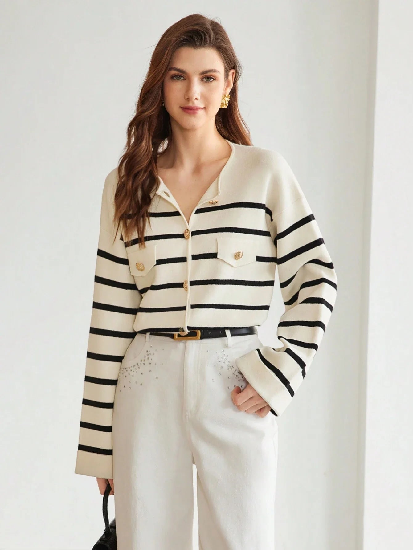 Cardigan blanc à rayures noires avec boutons dorés, poches à rabat, porté avec un pantalon blanc et ceinture noire, pour un style chic et intemporel.