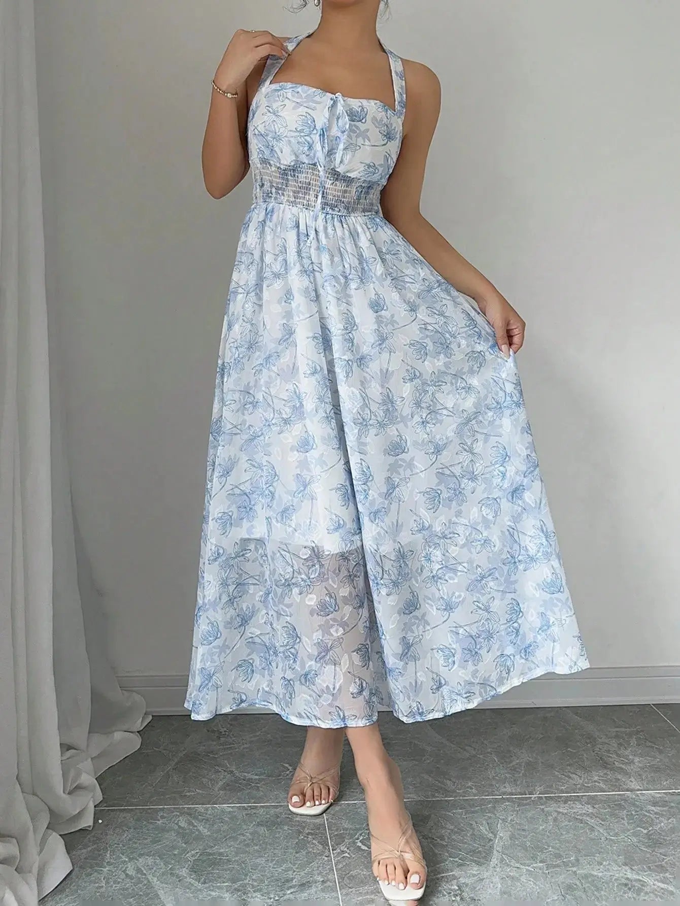 Robe longue bohème en polyester léger, imprimée floral bleu ciel. Encolure ras-du-cou, dos-nu, et buste froncé pour une silhouette élégante. Taille haute élastiquée et coupe évasée pour confort. Longueur jusqu'aux chevilles, doublée pour opacité. Lavage en machine ou nettoyage à sec recommandé.